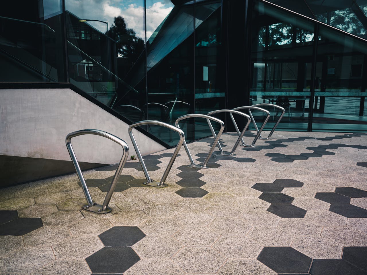 why-choose-us Contemporary bicycle racks set against the glass facade of a modern office building, featuring geometric pavement patterns.